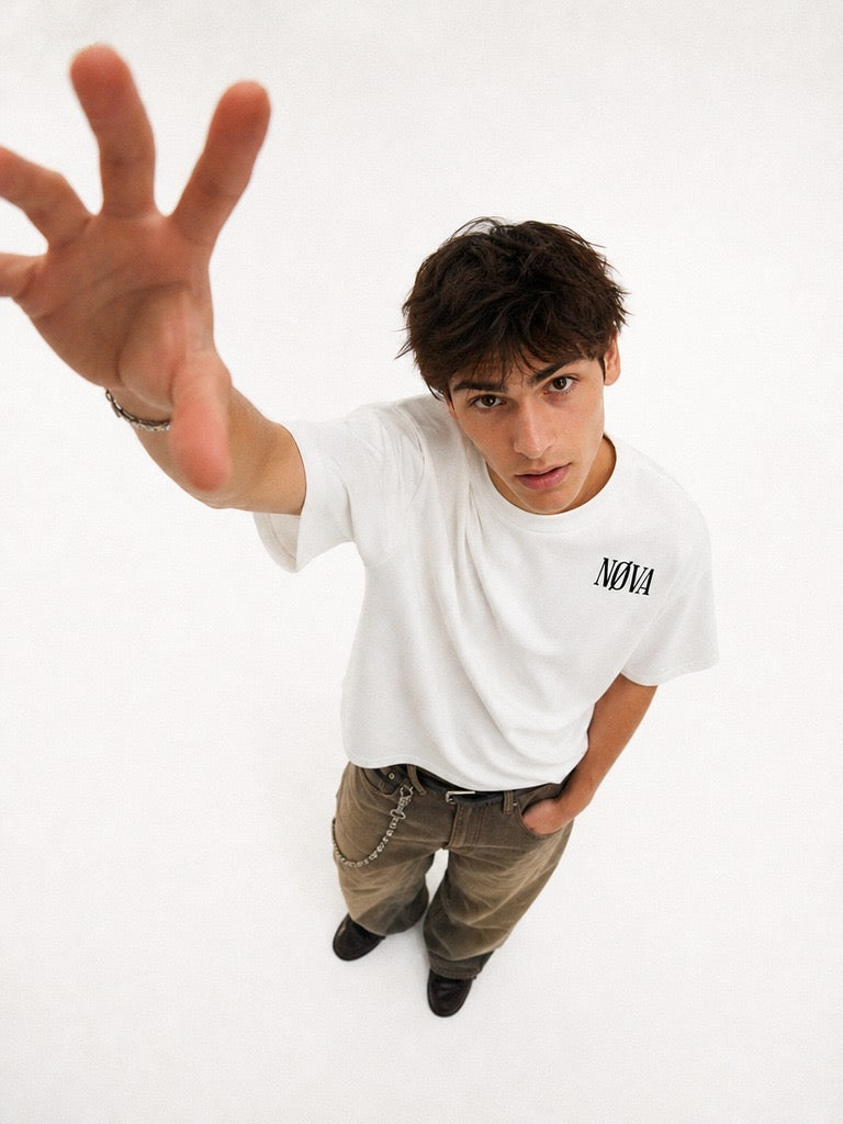 Model im weißen NØVA T-Shirt vor weißem Hintergrund, Hand zur Kamera
